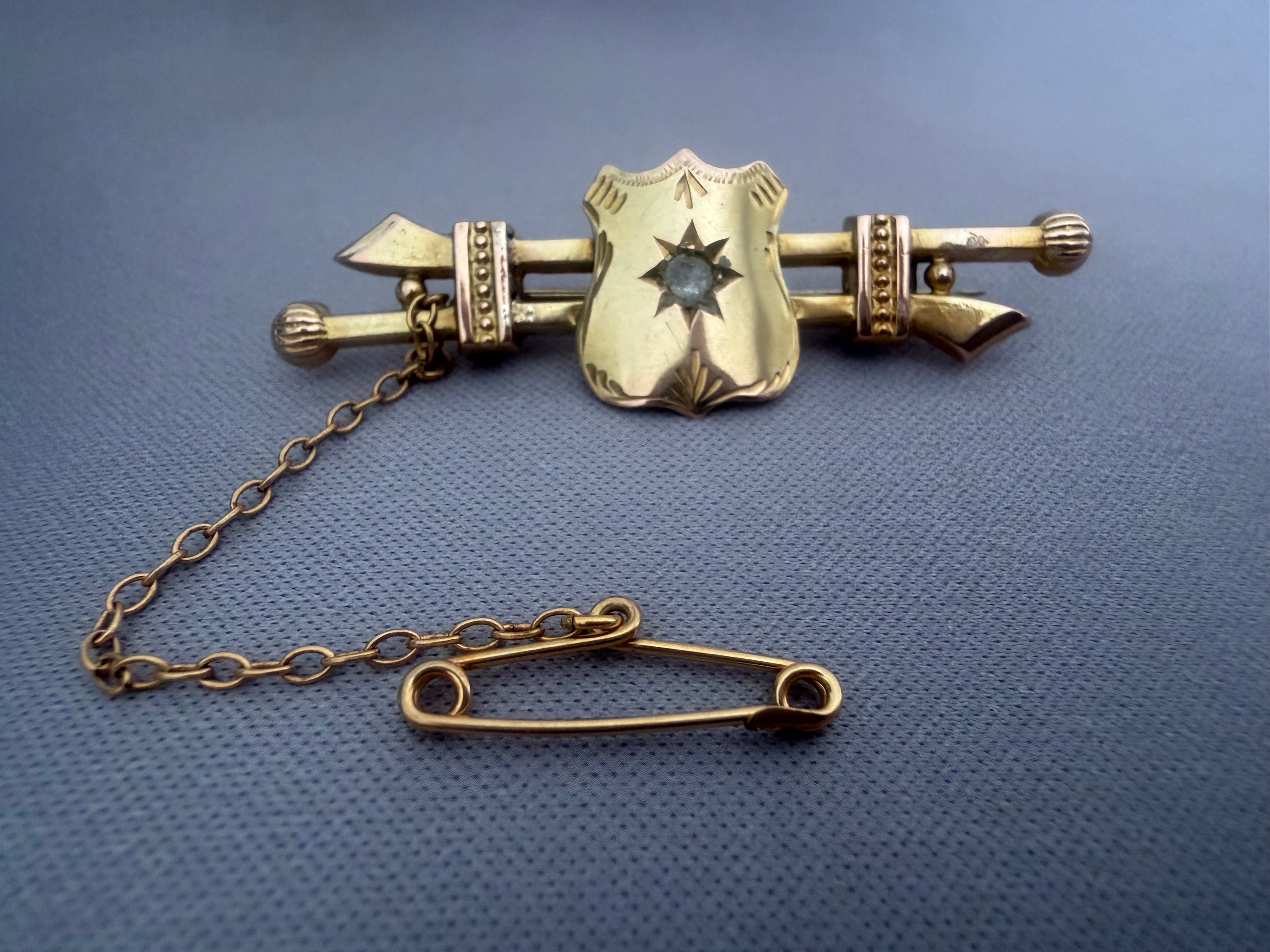 Antique Australian Gold brooch with shield design and chain on a blue textured background.  Aronson & Co