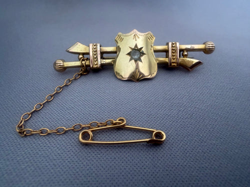 Antique Australian Gold brooch with shield design and chain on a blue textured background.  Aronson & Co