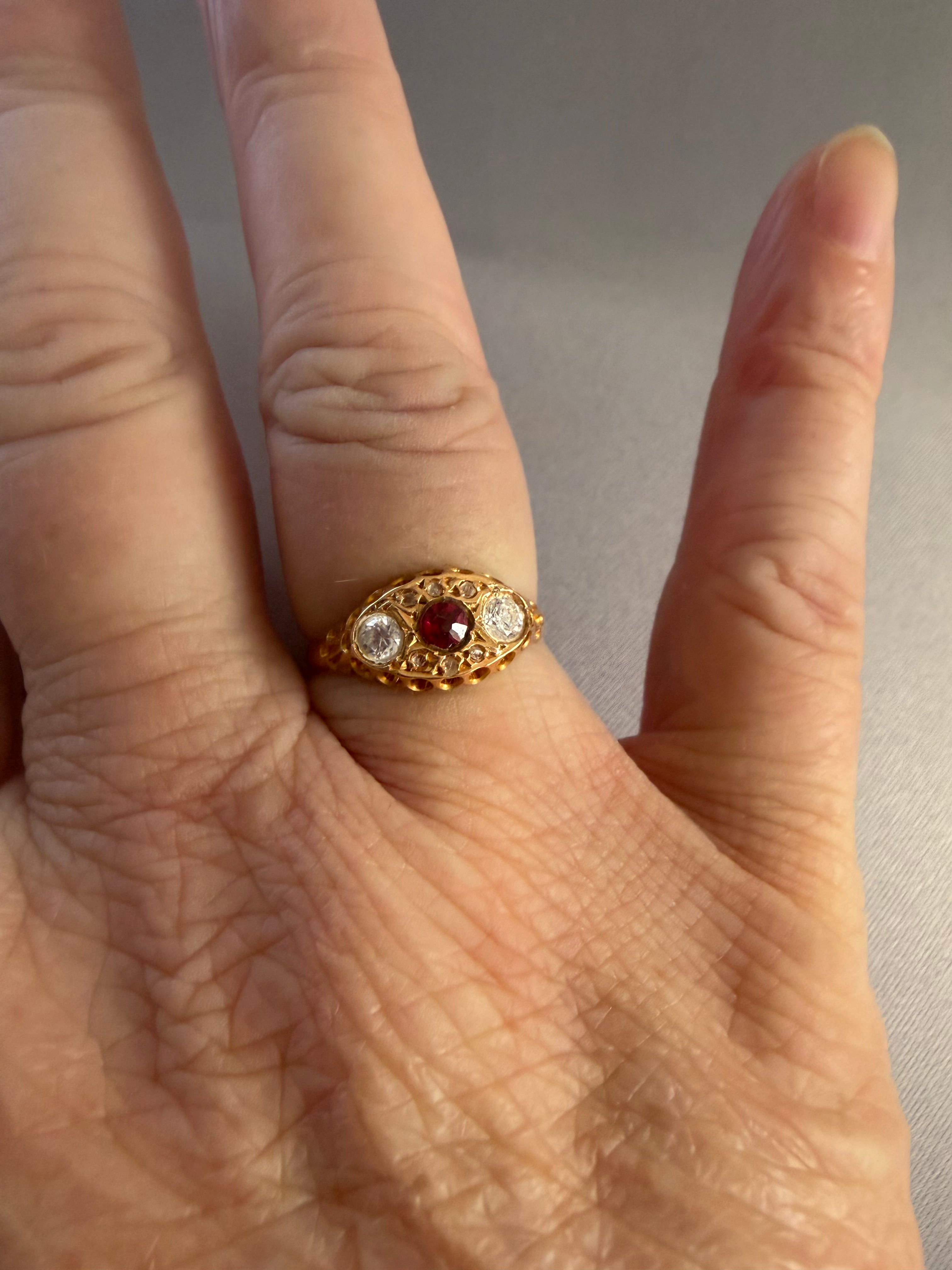 18ct Antique Victorian Gold ring with a red gemstone and smaller clear stones on a gray textured background.  Ring on ladies finger